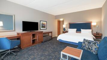 Habitación de hotel con cama, escritorio con televisor, una silla, una mesita y un sofá.