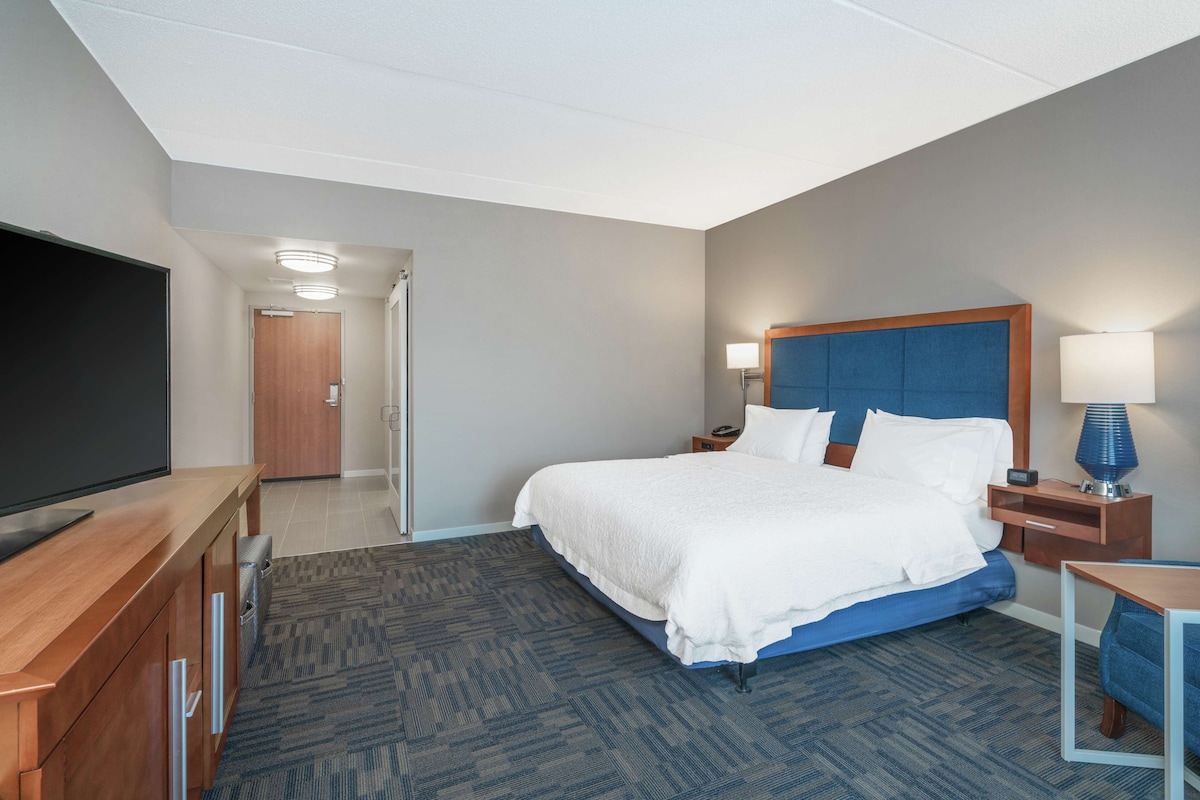 A hotel room with a large bed, a TV, a desk, and a lamp.