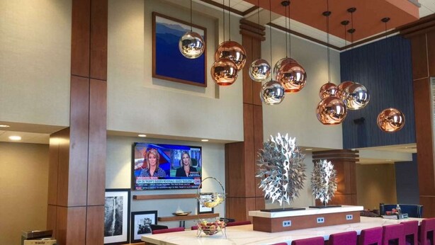 A hotel lobby with a reception desk, bar area, and a television displaying news.