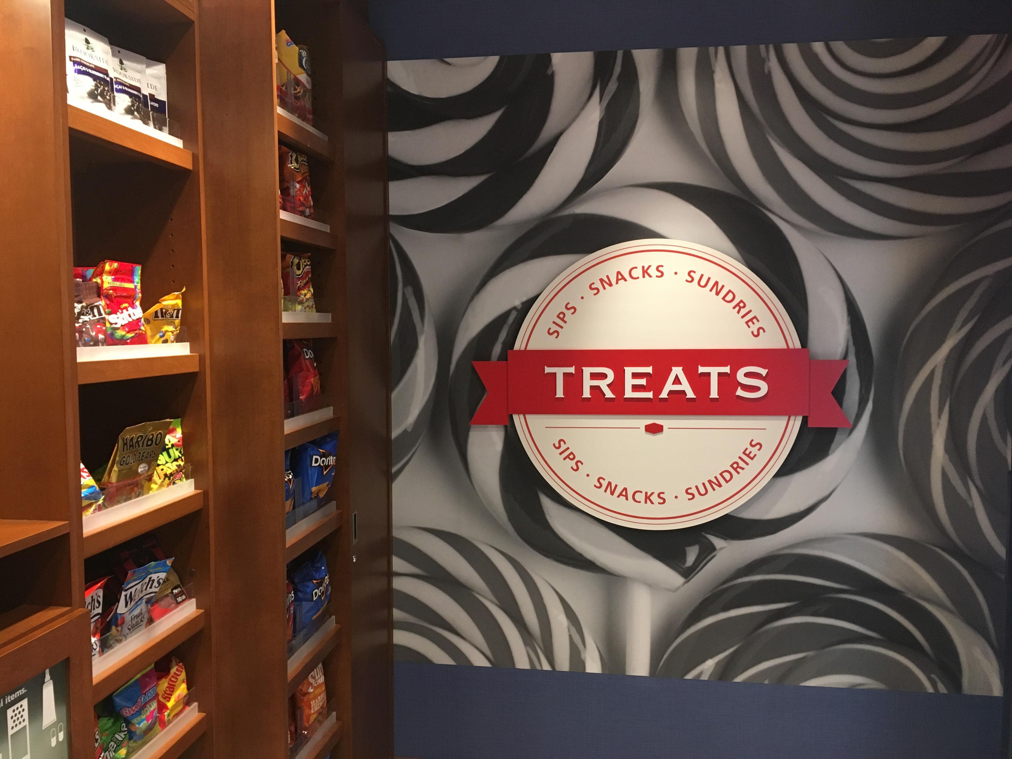 Een muur met een rond bord waarop 'TREATS' staat, omringd door planken vol snacks.
