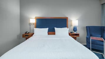 A hotel room with a large bed, two bedside tables, a chair, and a nightstand with a lamp.