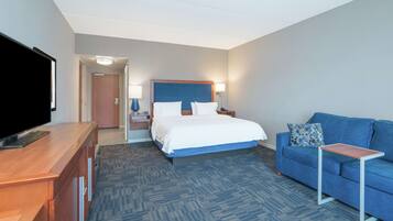 A hotel room with a bed, a blue sofa, a TV, a desk, and a lamp.