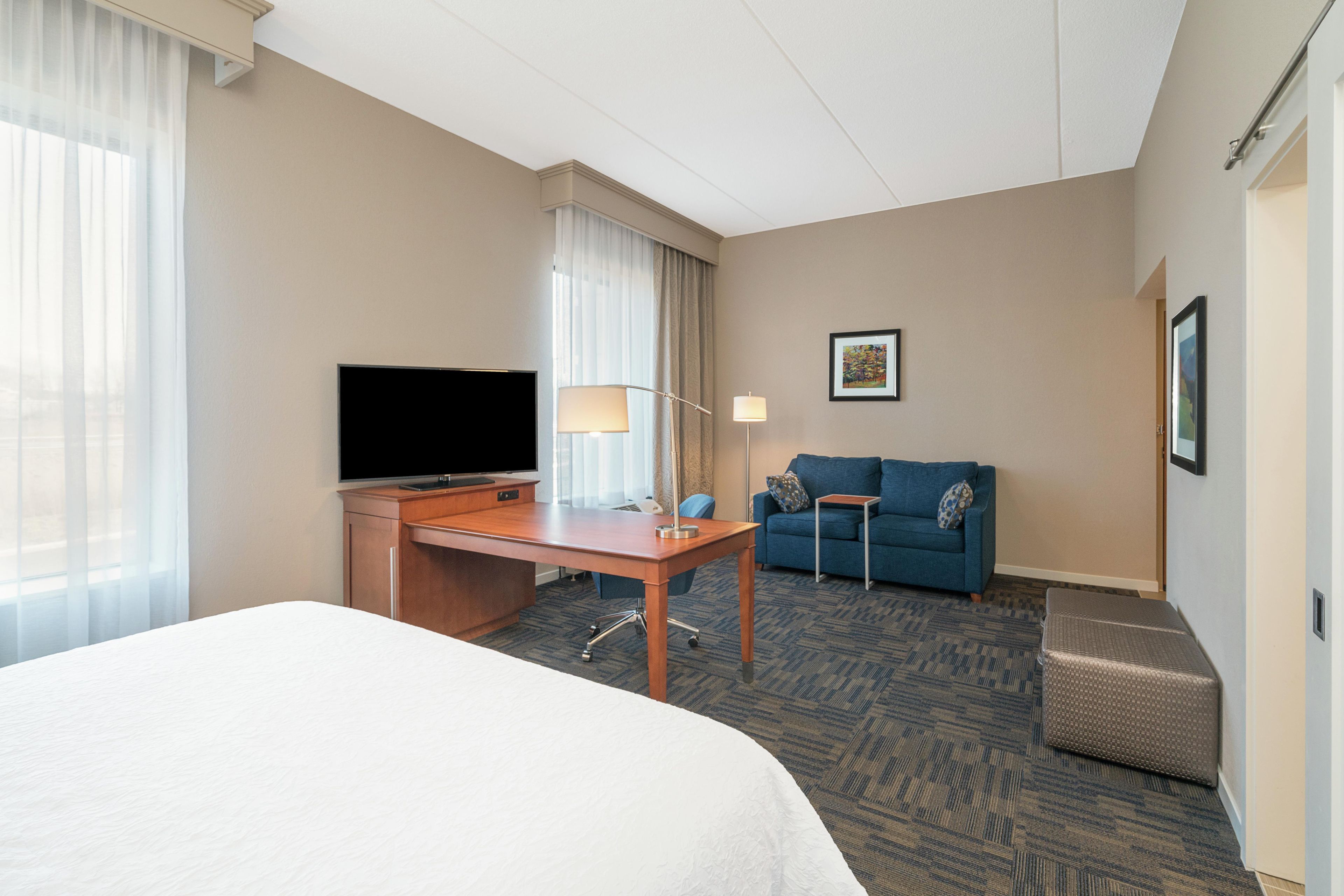 Une chambre d’hôtel avec un lit, un bureau doté d’un téléviseur à écran plat, un canapé bleu, une petite table et une lampe.