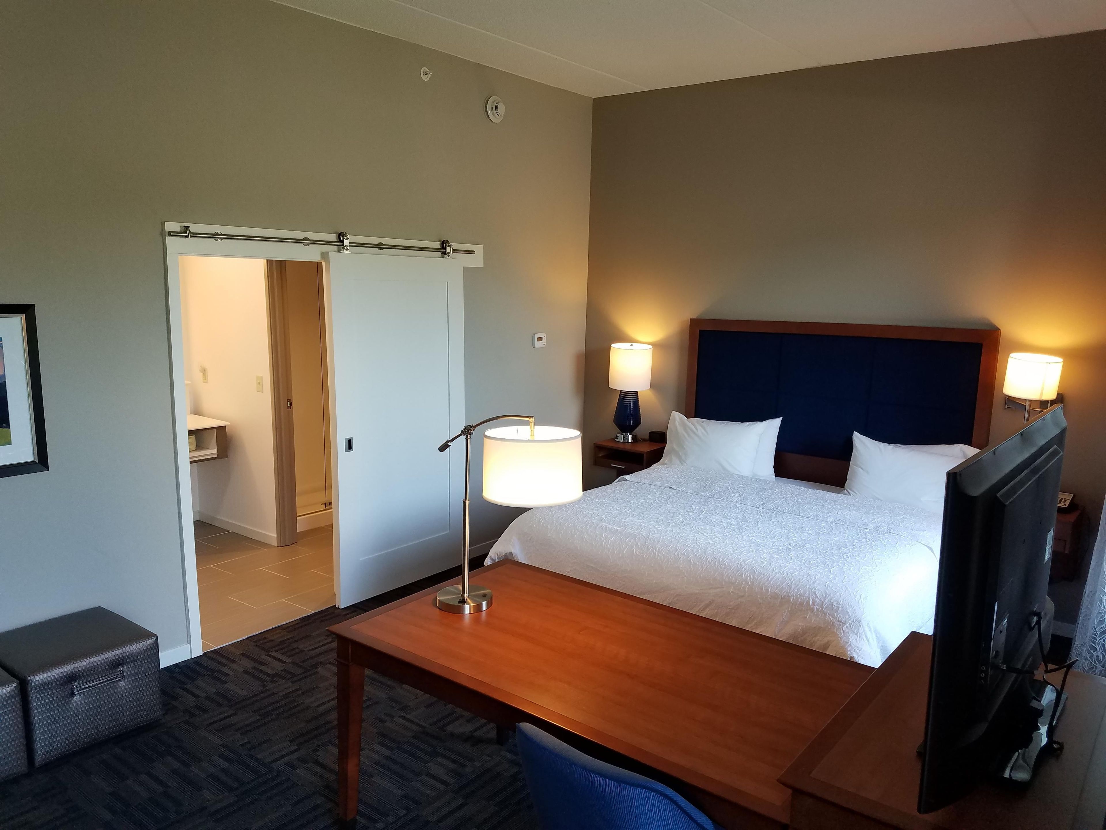 A hotel room with a bed, bedside lamps, a desk, a television, and a door leading to a bathroom.