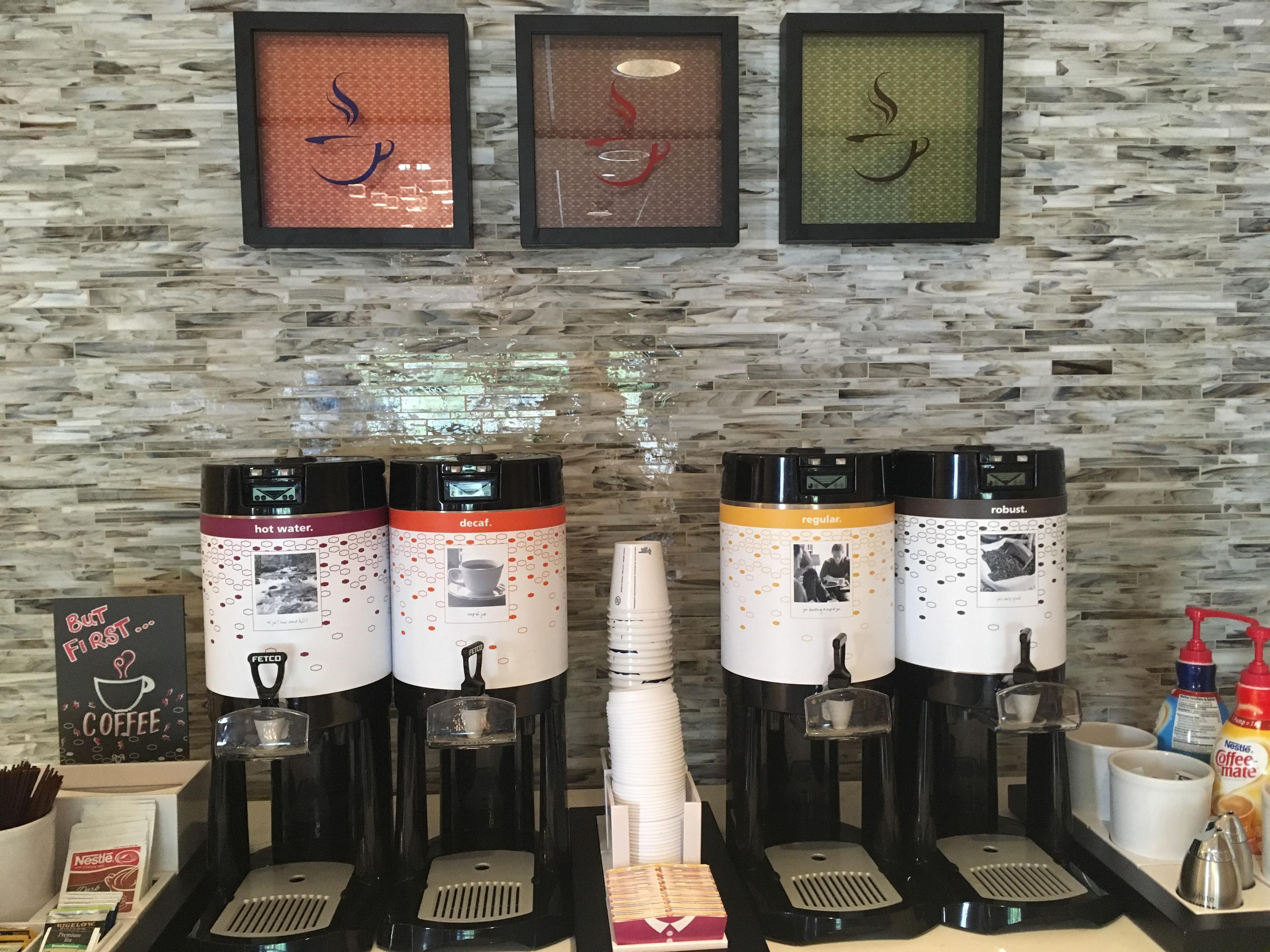 Kaffestation med flere dispensere, et skilt og en væg med et struktureret mønster.