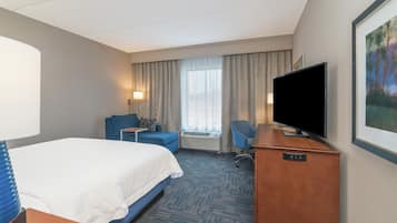 A hotel room with a bed, a desk, a chair, a television, and a window with curtains.