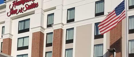 A Hampton Inn & Suites hotel building with a prominent American flag.