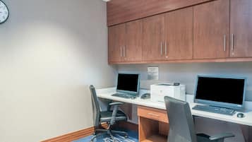 A hotel office with two desks, computers, chairs, and a clock on the wall.