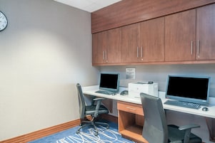 A hotel office with two desks, computers, chairs, and a clock on the wall.