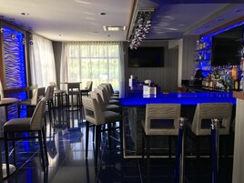 A bar area with a long counter, multiple bar stools, and a variety of bottles.