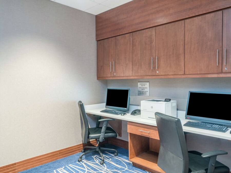 A hotel office with two desks, computers, chairs, and a clock on the wall.