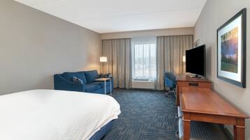 A hotel room with a bed, a desk, a chair, a television, and a window with curtains.
