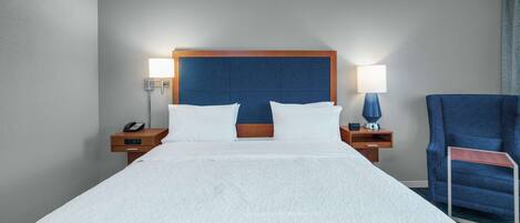 A hotel room with a large bed, two bedside tables, a chair, and a headboard.