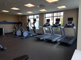 Et fitnesscenter med løbebånd, crosstrainere og et stort vindue med udsigt til bygninger.