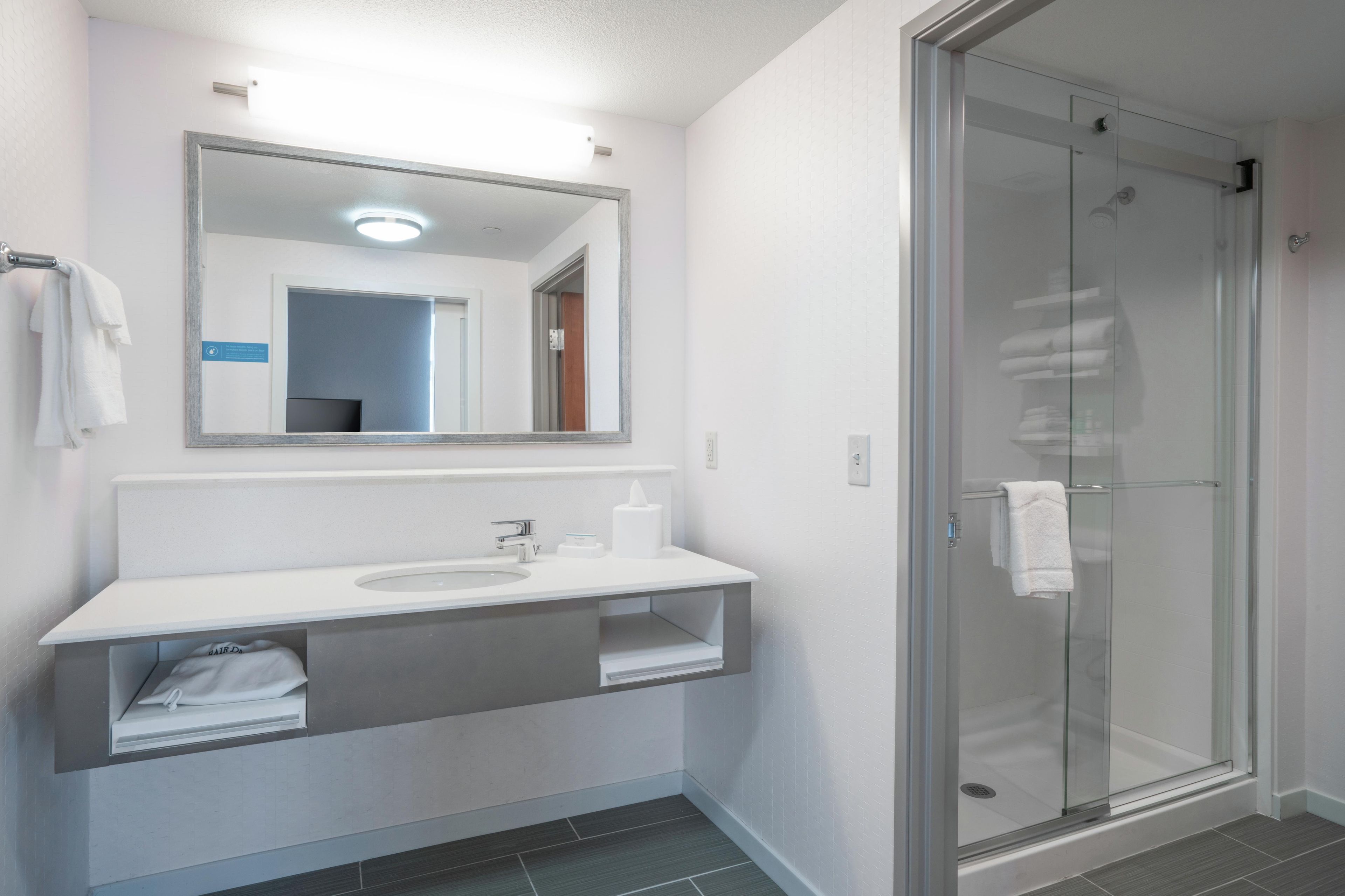 A modern bathroom with a glass shower enclosure, a white sink with a vanity, and a mirror above the sink.