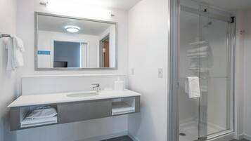 A modern bathroom with a glass shower enclosure, a white sink with a vanity, and a mirror above the sink.