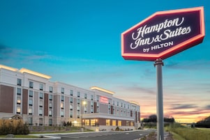 A Hampton Inn & Suites by Hilton hotel with a large illuminated sign, modern architecture, and a well-lit facade.