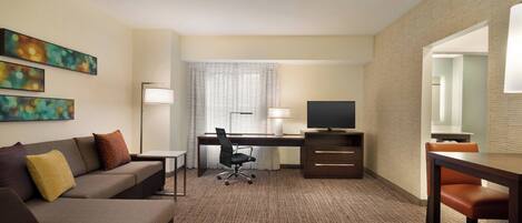 Een hotelkamer met een bank, bureau, televisie en kunstwerk aan de muur.