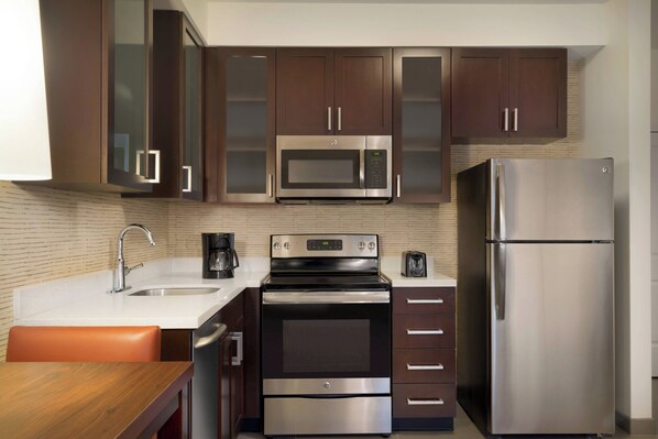 Una cocina moderna con electrodomésticos de acero inoxidable, armarios de madera oscura y encimera blanca.