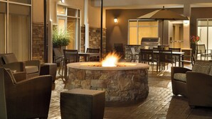Un patio al aire libre con suelo de piedra, mobiliario de mimbre, una chimenea central y una parrilla.
