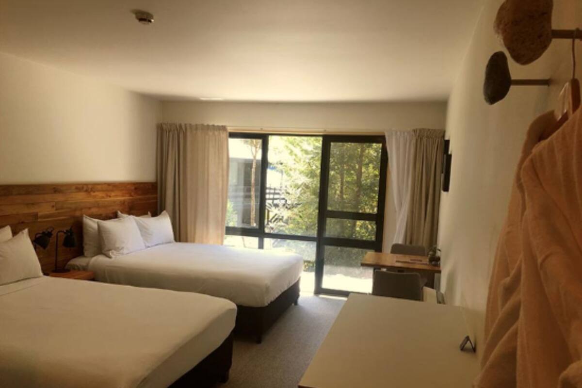 A hotel room with two beds, a desk, and a large window.
