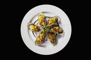A white plate with mussels arranged in a circular pattern, garnished with green herbs and a small purple flower. - Maruia Hot Springs (Lewis Pass)