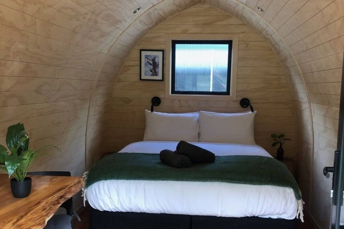 A cozy, arched wooden room with a bed, a small window, and a plant.