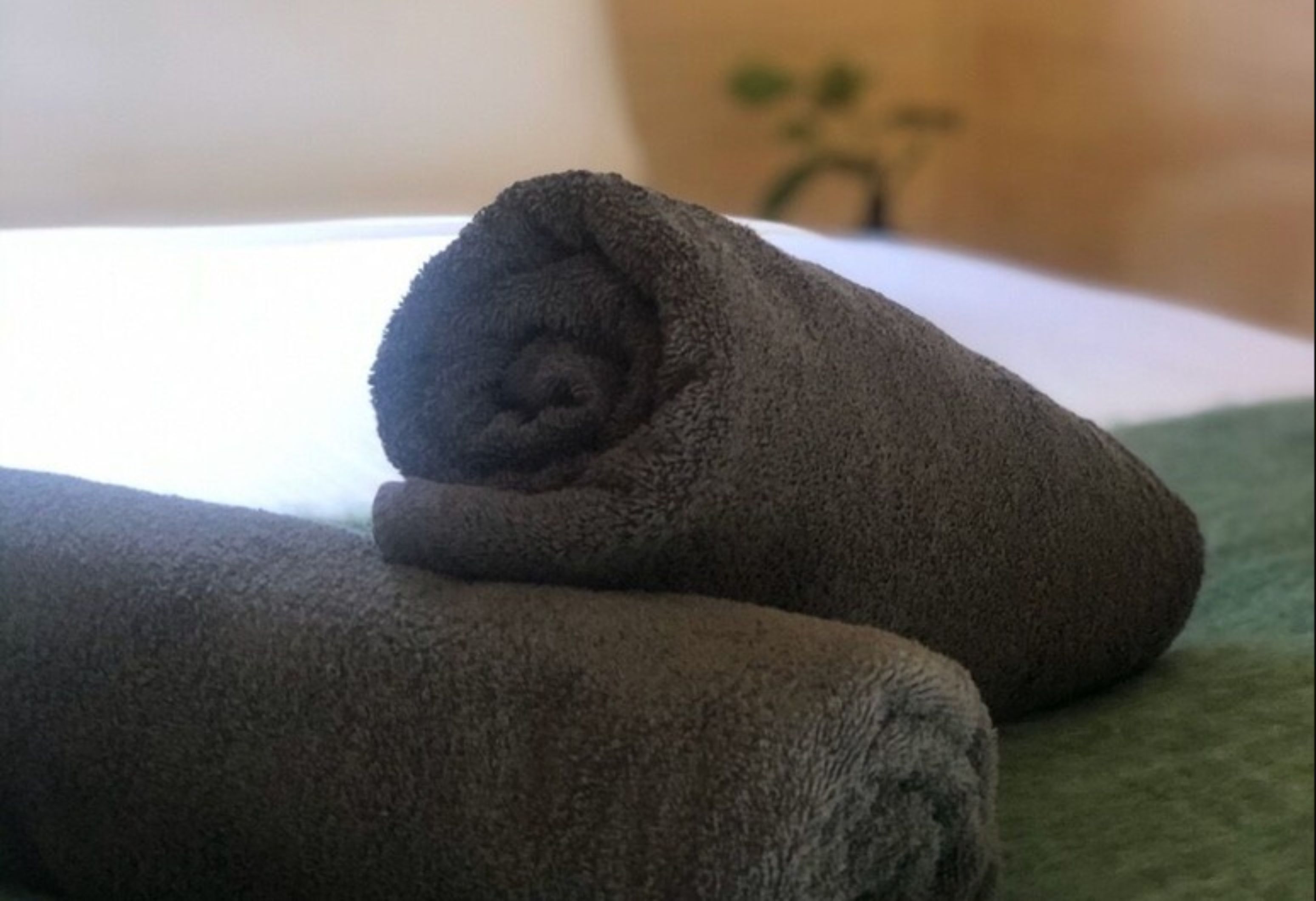 A neatly folded dark-colored towel on a green surface, likely a bed or a towel rack.