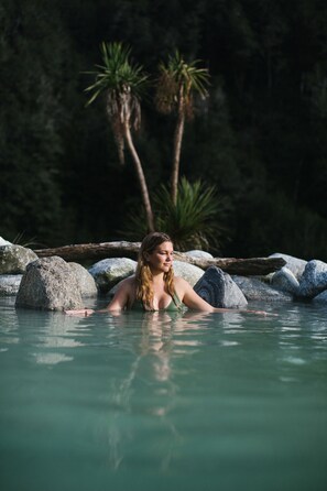 A person in a natural pool surrounded by rocks and trees. - Maruia Hot Springs (Lewis Pass)
