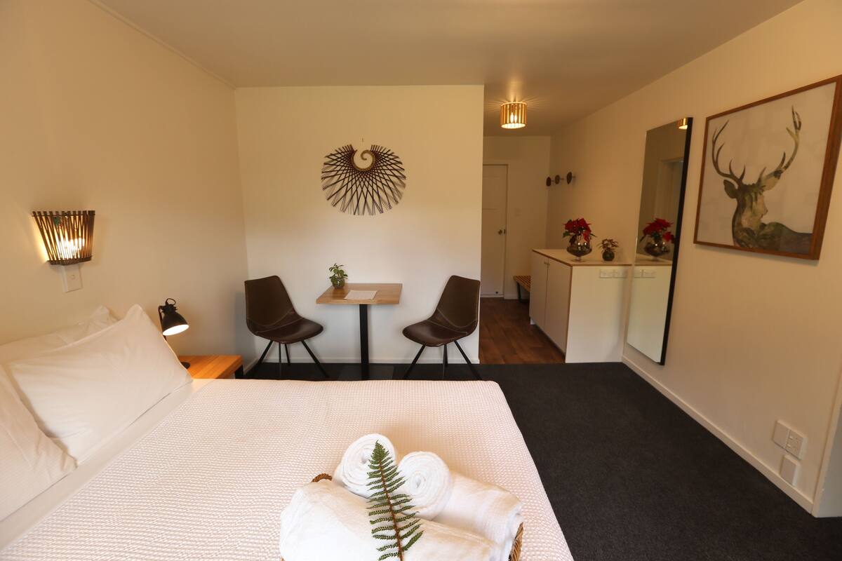 A hotel room with a large bed, two chairs, a small table, and a mirror.
