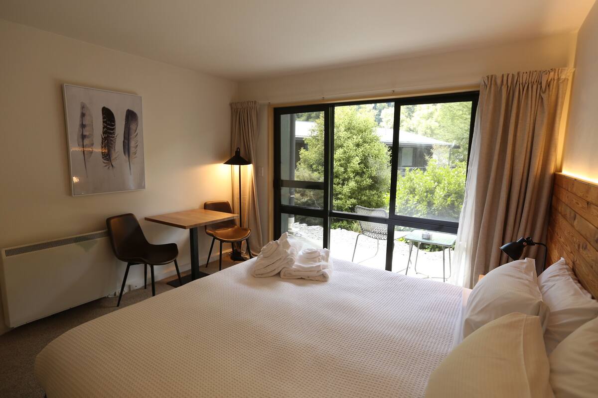 A hotel room with a large bed, a desk, a chair, and a view of the outdoors.