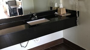 A bathroom with a black countertop, a sink, a mirror, a hairdryer, and a telephone. - Moonlight Inn (Houston)