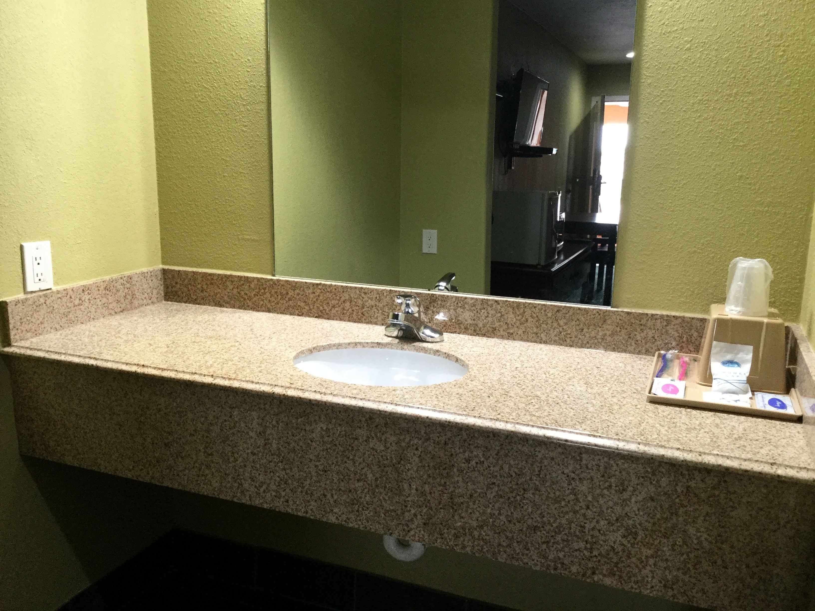 Une salle de bain avec un comptoir en granit, un lavabo, un miroir et une petite boîte contenant des articles de toilette.