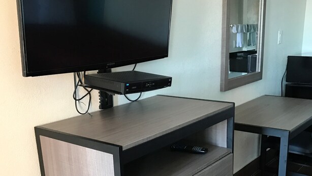 A modern hotel room with a flat-screen TV mounted on a wooden cabinet, a mirror above the TV, and a small table with a chair. - Moonlight Inn (Houston)
