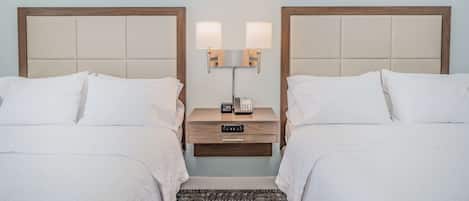 Una habitación de hotel con dos camas, una mesita de noche con lámpara, teléfono y un cajón pequeño.