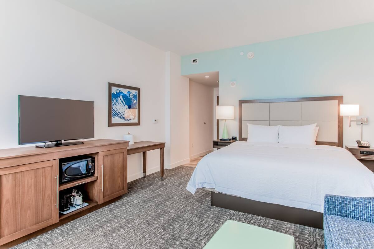 Een hotelkamer met een bed, een televisie, een bureau en een schilderij aan de muur.