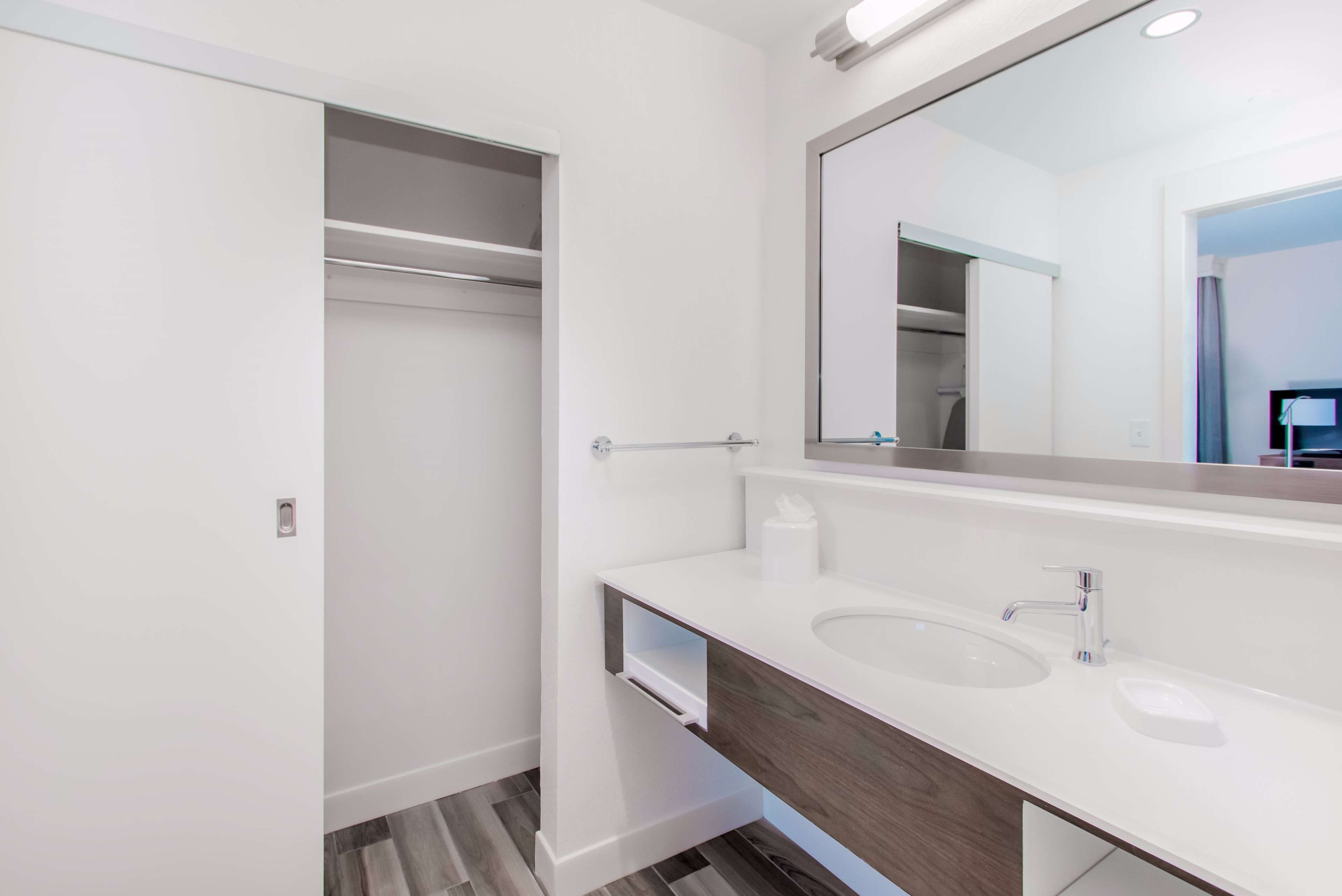 A modern bathroom with a white vanity, a large mirror, and a walk-in closet.