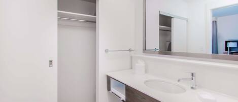 A modern bathroom with a white vanity, a large mirror, and a walk-in closet.