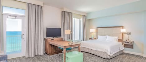 Una camera d'albergo con un letto, una scrivania, una sedia e vista sull'oceano attraverso una porta scorrevole.