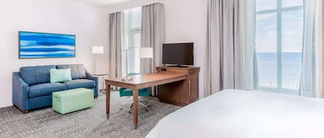 Ein Hotelzimmer mit einem Bett, einem Schreibtisch mit Fernseher, einer Couch und Meerblick.