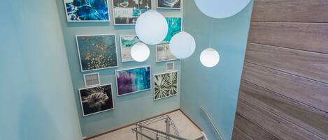 A staircase with a metal handrail, a light blue wall with various framed artworks, and a wooden panel on the right.