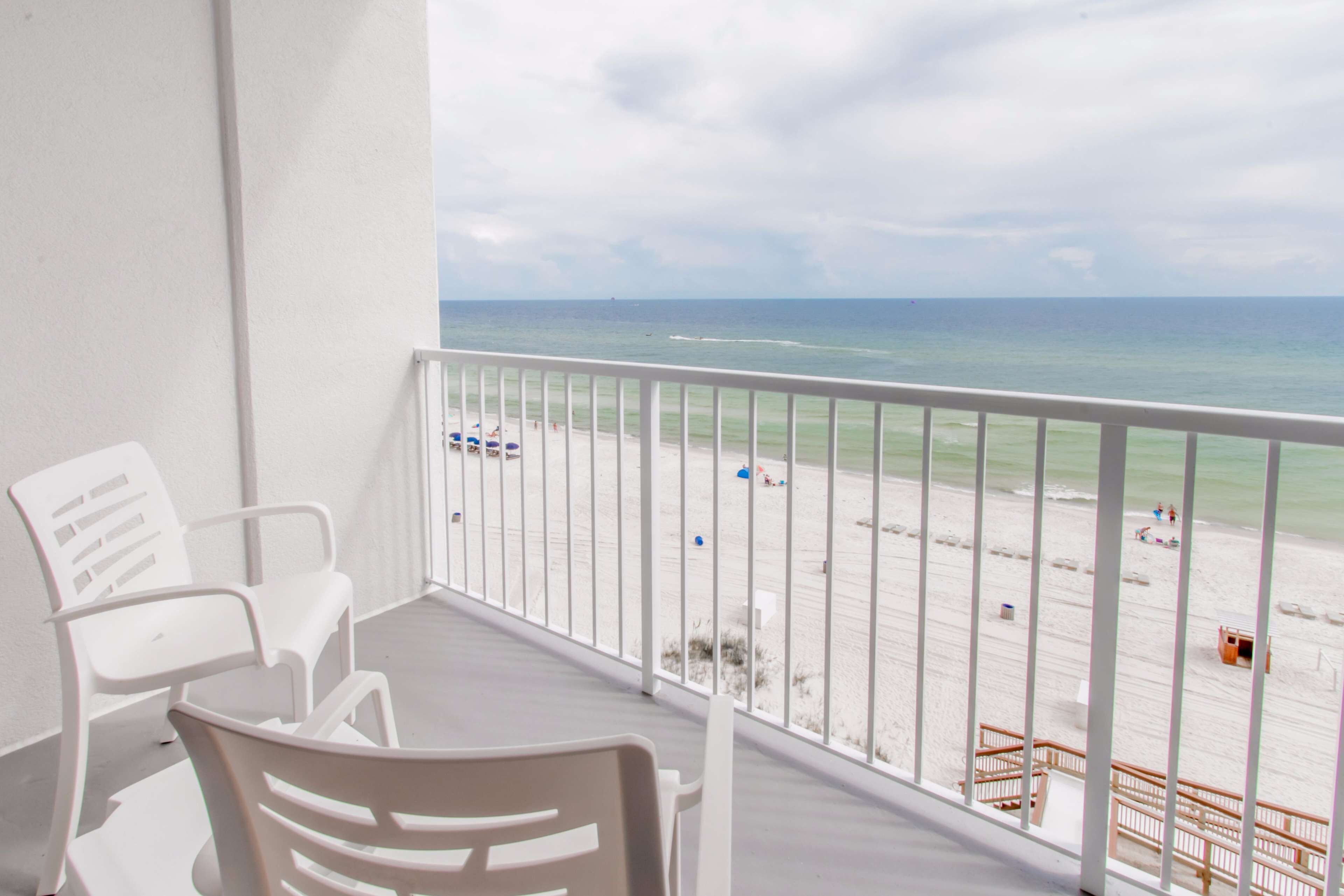 A balcony with white chairs and a view of the beach.