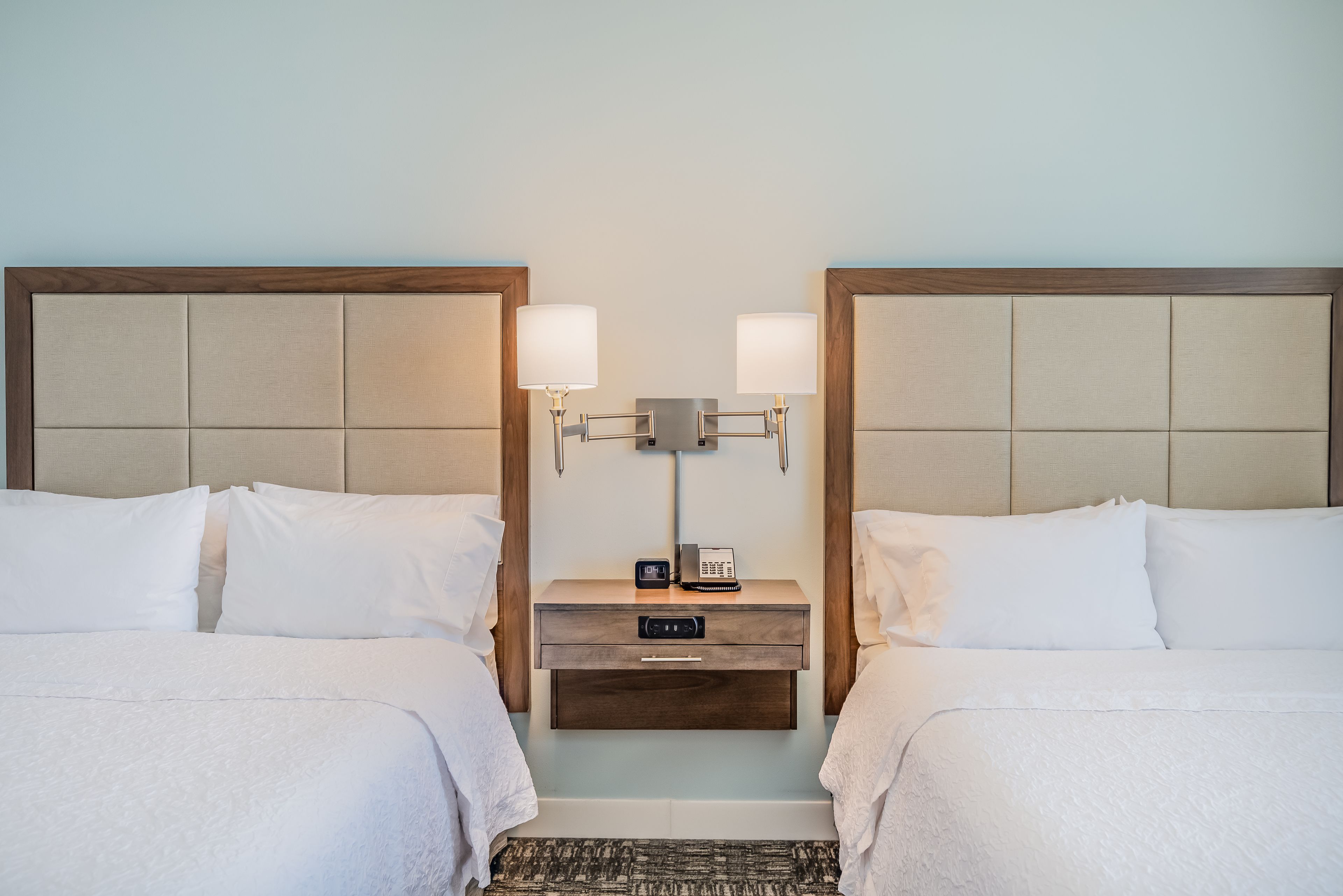 Une chambre d’hôtel avec deux lits, une table de chevet avec une lampe et un téléphone.