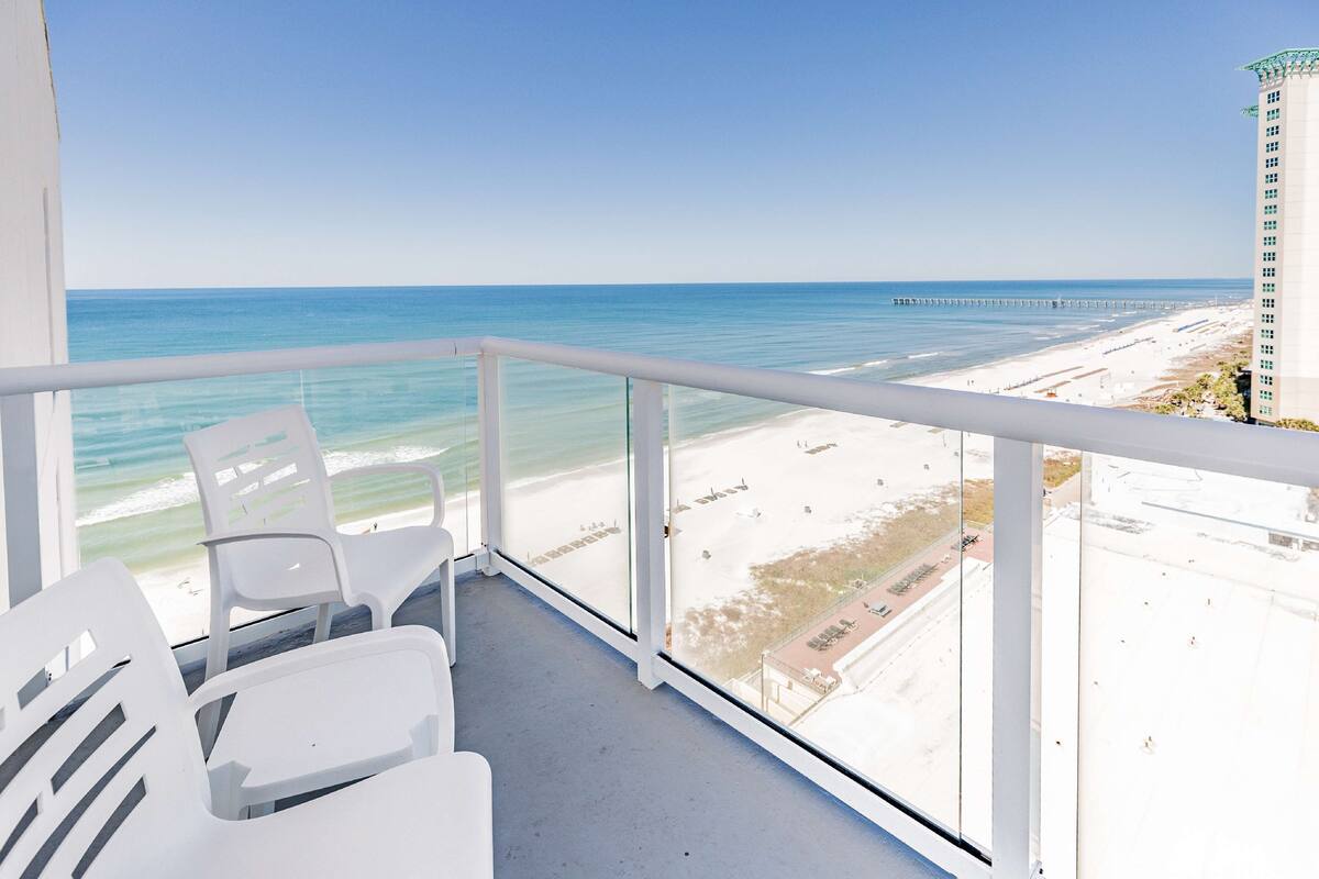 Een balkon met witte stoelen met uitzicht op een strand en een pier.