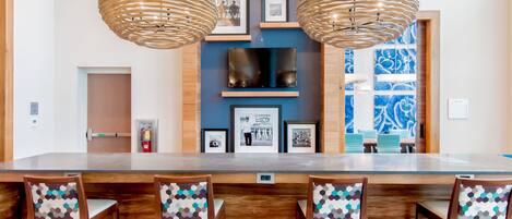 Een bar met houten stoelen en een lange bar. Twee hangende lampen en een flatscreen televisie aan de muur.