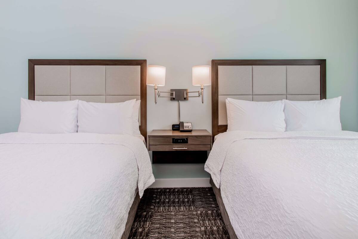 Een hotelkamer met twee bedden, elk voorzien van een hoofdeinde, een nachtkastje met een lamp en een telefoon.