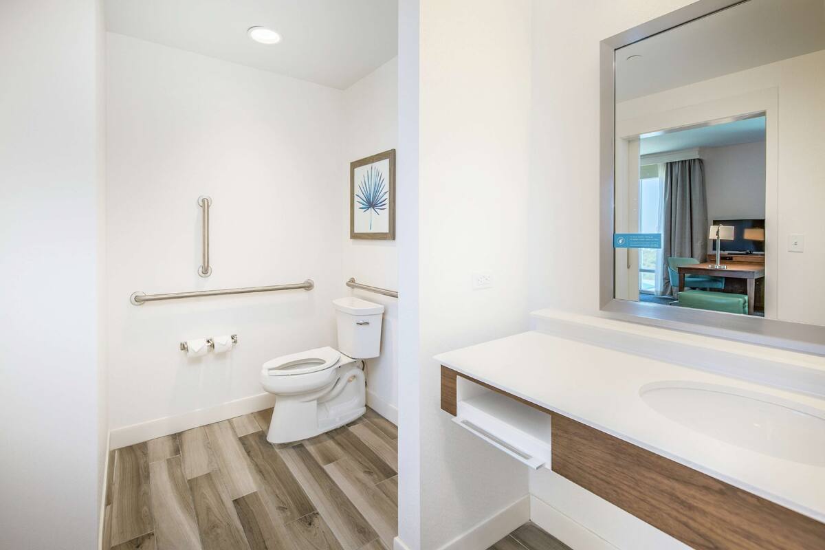 Een moderne badkamer met toilet, handgrepen, wastafel en spiegel.