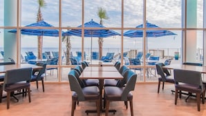 Un salón de conferencias con un amplio ventanal que da a una zona de piscina con sombrillas y sillas azules.