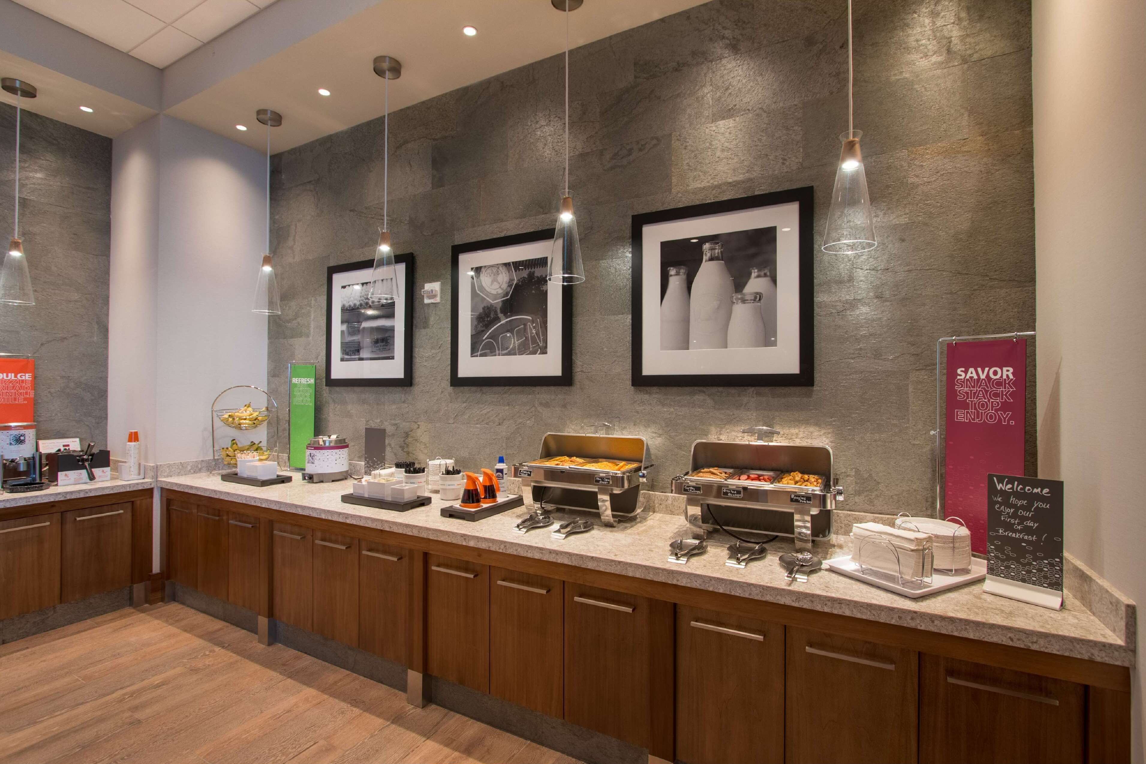 A breakfast bar with various food items, framed pictures on the wall, and a welcome sign.