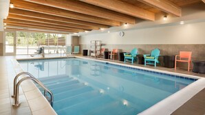 Une piscine intérieure avec des poutres en bois, un sol carrelé et des fauteuils Adirondack aux couleurs vives.